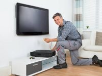 Full length of male technician installing TV set top box at home